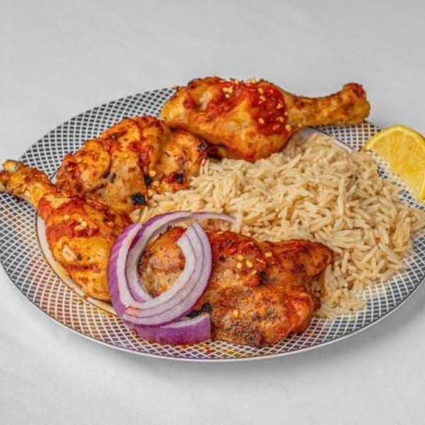 Four pieces of grilled chicken with rice, red onion slices, and a lemon wedge on a patterned plate.